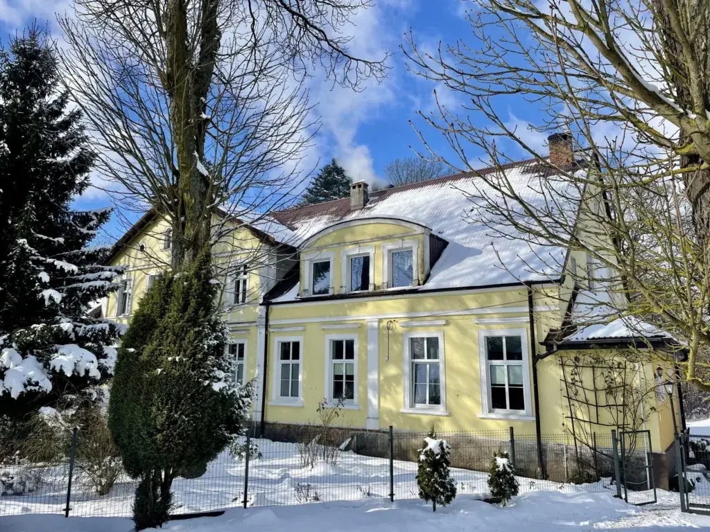Żółty dom Ośrodka MONAR w Kamieniu Rymańskim w zimowej scenerii, dach i ogród pod śniegiem