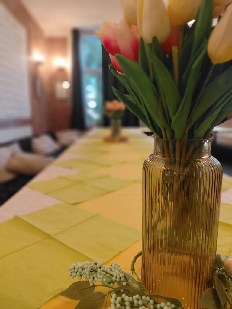Szklany wazon z tulipanami na stole nakrytym żółtymi serwetkami, przygotowanym na święto